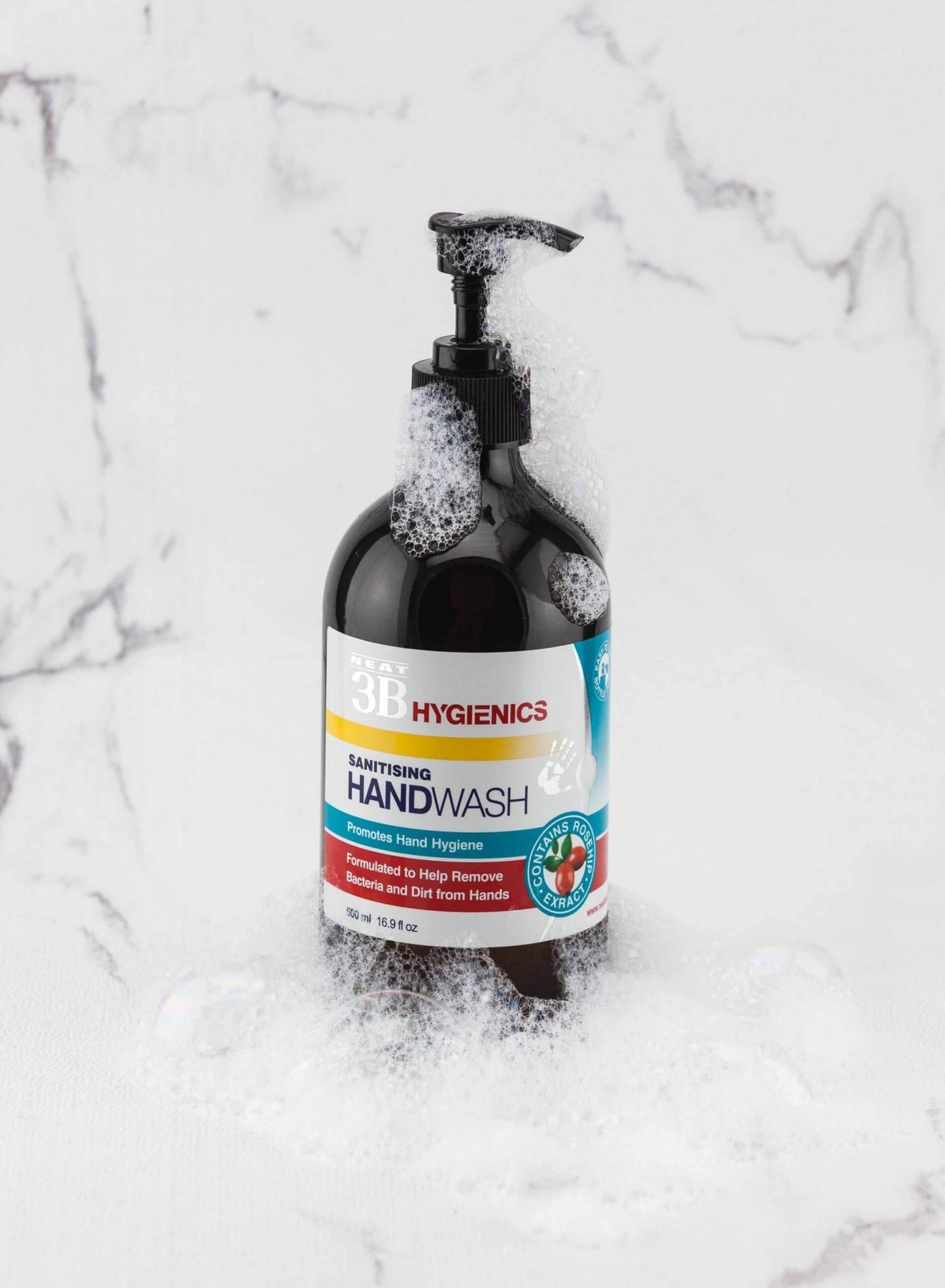 Neat Feat Hygienics Sanitising Handwash, front-on in a dark brown bottle with a black cap, featuring a white label with blue and red accents, placed on a white marble background with foam on the bottle.