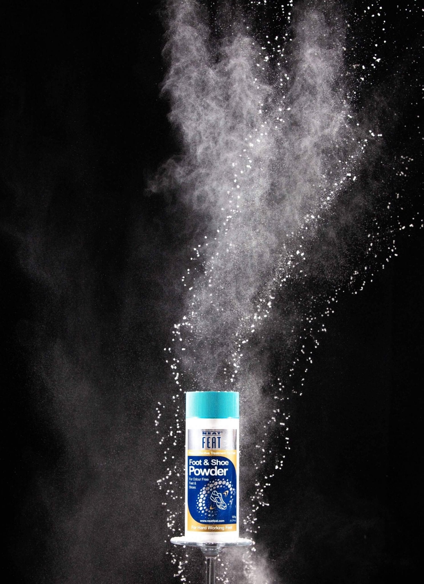 Neat Feat Foot & Shoe Powder displayed on a small table with a black background, featuring an explosion of powder behind the product.